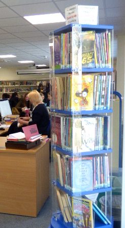 A photograph of our library facility featuring students reading, the librarian at her desk and a large display of books