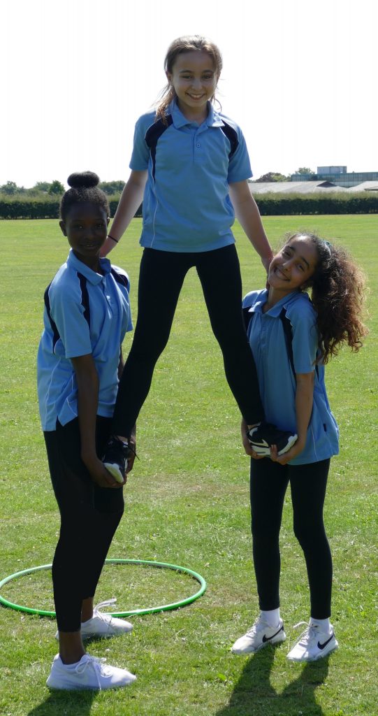 Two students support a third, standing in their hands in a pyramid form. All wearing the smart blue and black PE Kit uniform